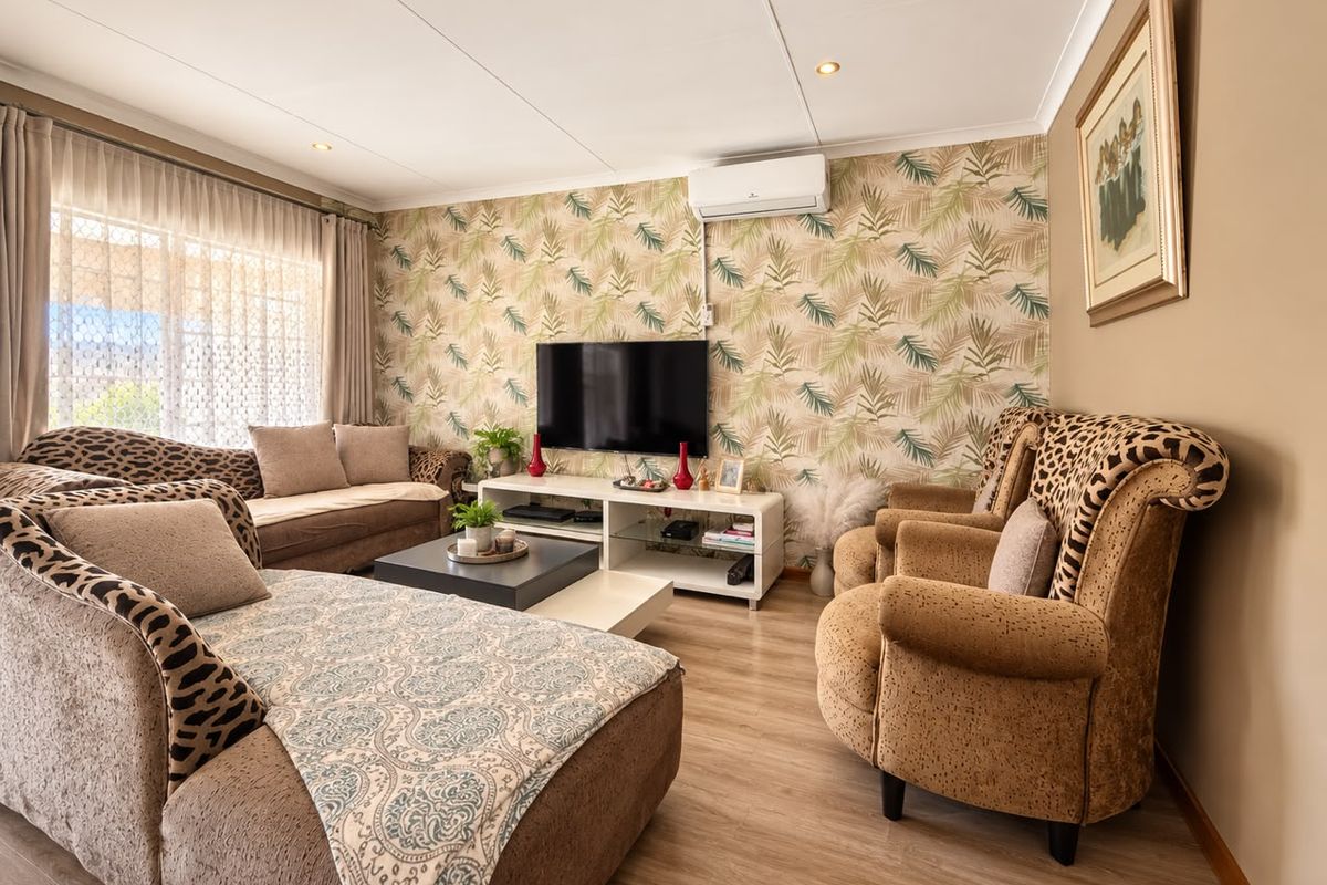 A well-maintained living room featuring laminate flooring, a split-system air conditioner, and a decorative wallpaper feature wall.