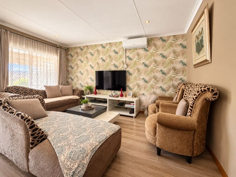 A well-maintained living room featuring laminate flooring, a split-system air conditioner, and a decorative wallpaper feature wall.