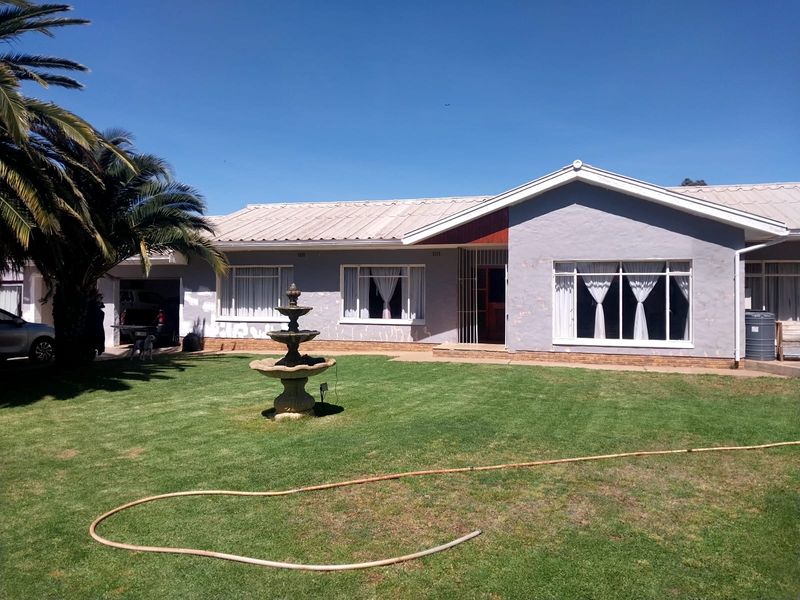 Front view of a single-story house featuring a metal roof, large windows, and a front garden with a fountain.