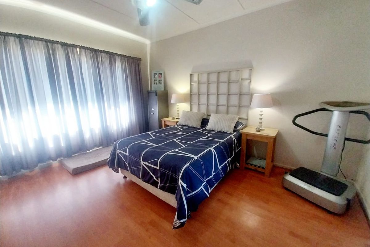 A spacious bedroom featuring laminate flooring, a ceiling fan, and large windows with full-length curtains, offering a comfortable and functional living space.