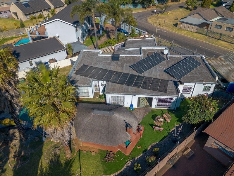 Aerial view of the property featuring a main house with solar panels, a detached thatched lapa, and a landscaped garden area.