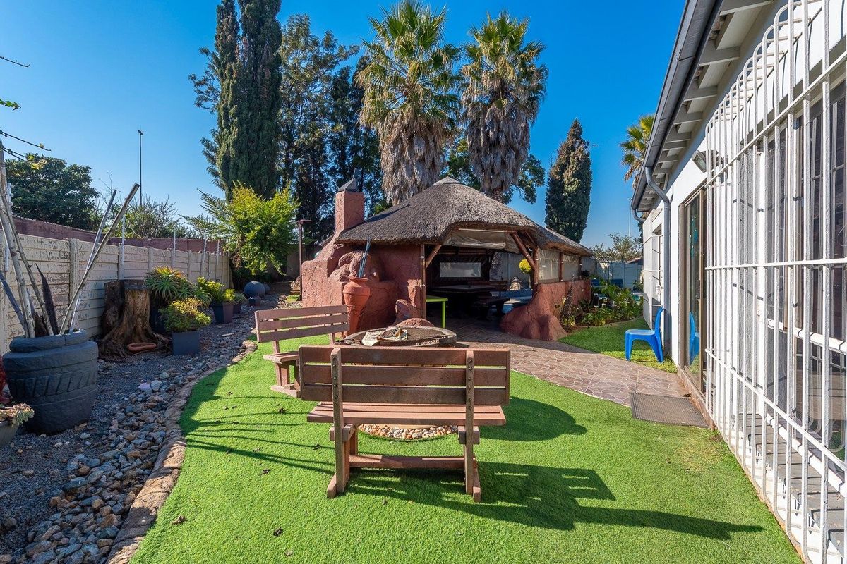 Rear garden area featuring an artificial lawn, paved walkway, and a traditional thatched lapa with a built-in braai facility.