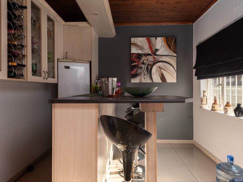 A compact kitchen featuring light wood cabinetry, a built-in wine rack, a breakfast bar, and a distinctive timber ceiling with tiled flooring.