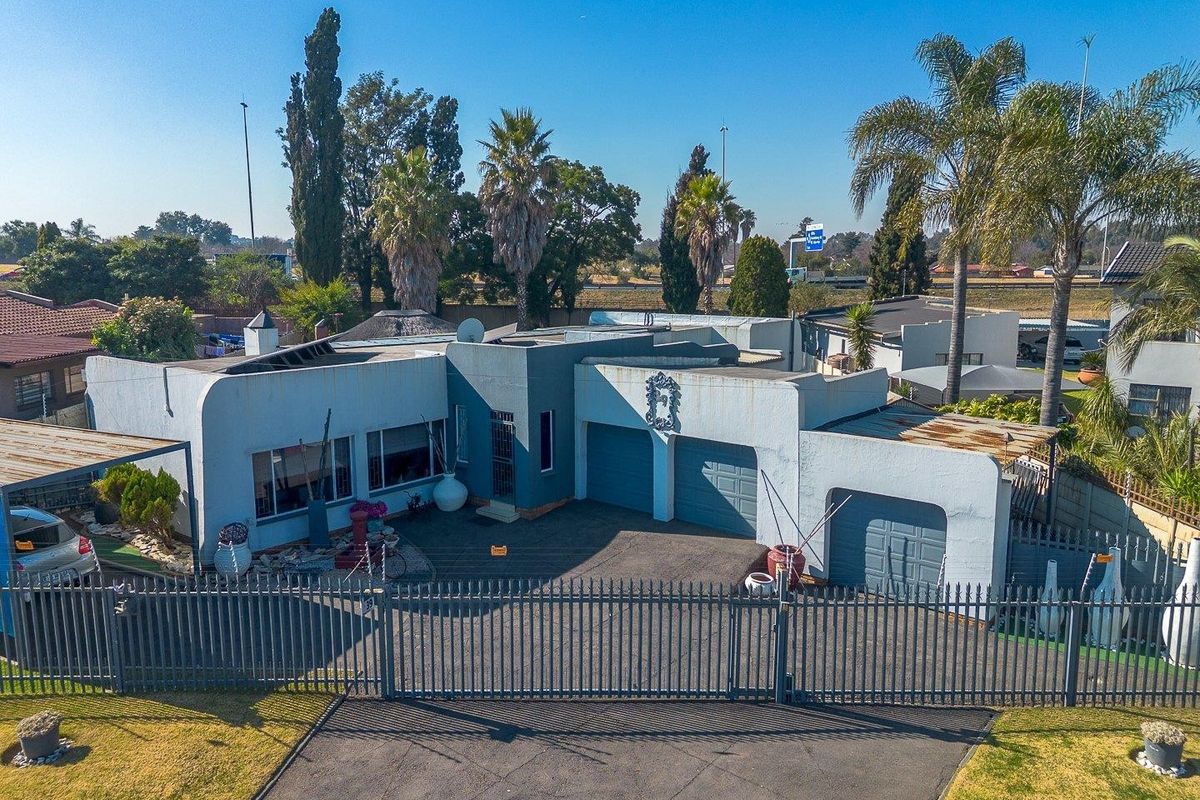 Aerial view of a residential property featuring a multi-car garage, paved driveway, and secure perimeter fencing, showing signs of exterior wear.