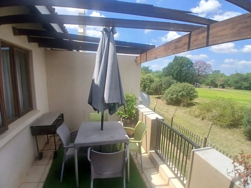 A covered balcony featuring a wooden pergola and metal balustrade, overlooking a green landscape.