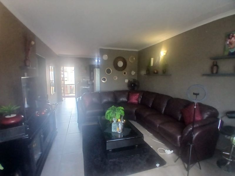 A living room area featuring tiled flooring and wall-mounted shelving, with a view leading towards an adjacent balcony area.