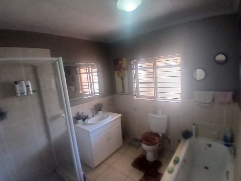 A functional bathroom featuring a separate shower enclosure, bathtub, vanity basin, and toilet, finished with tiled walls and floors.