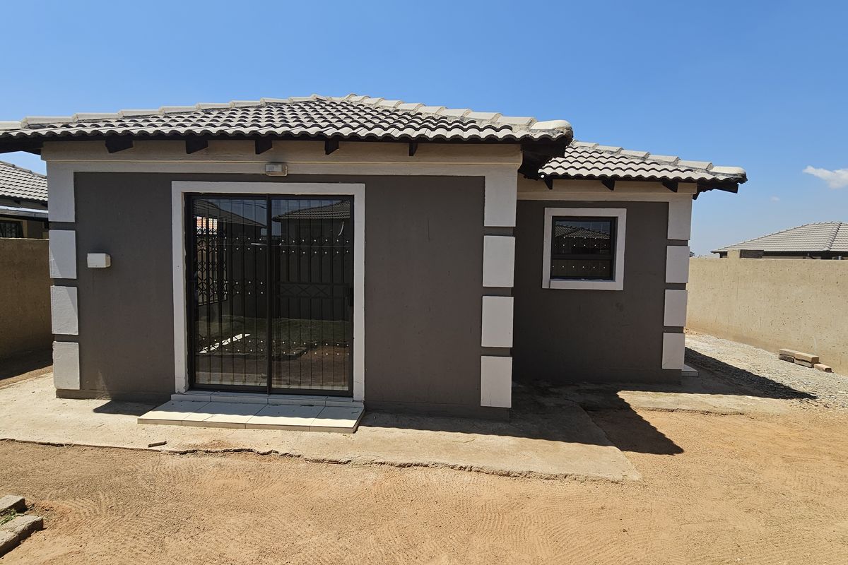 Rear view of a single-story house featuring a tiled roof, sliding glass door with security gate, and surrounding perimeter wall with unfinished yard space.
