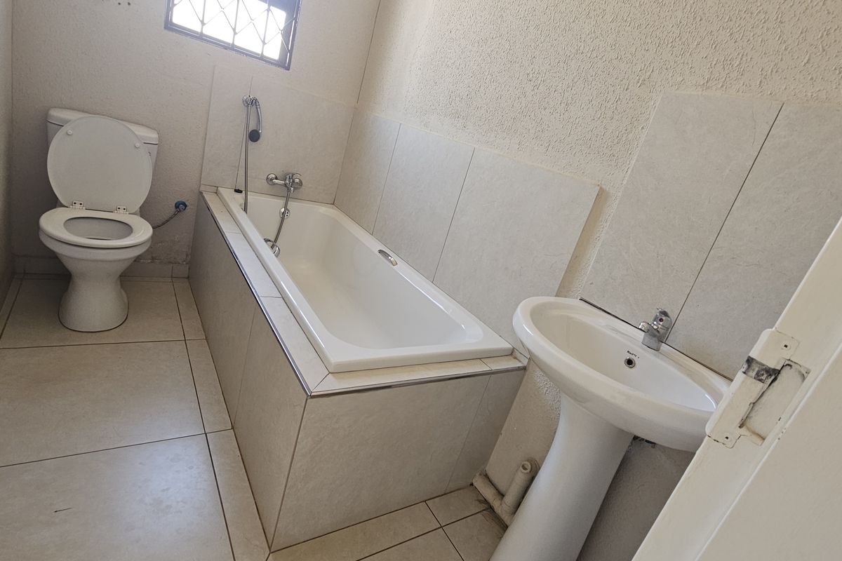 A functional bathroom featuring a pedestal basin, built-in bathtub, and toilet with neutral tiled finishes.