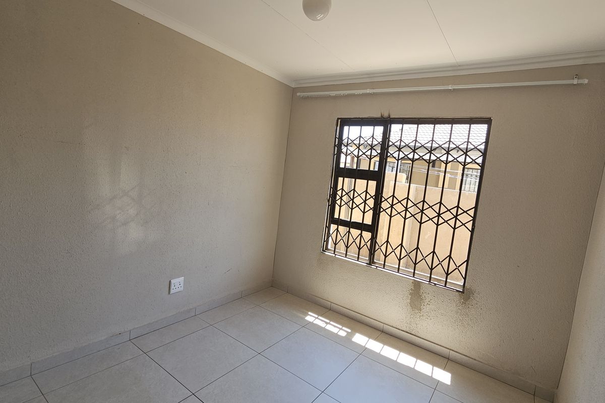 An empty bedroom featuring tiled flooring, security bars on the window, and a security gate, requiring minor maintenance to the wall finishes.