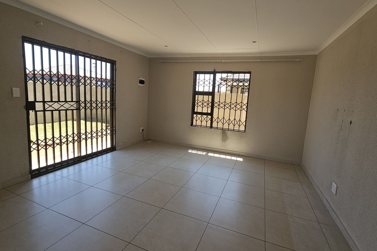 An empty living room featuring tiled flooring, security gates, and burglar bars, requiring minor cosmetic attention to the walls.