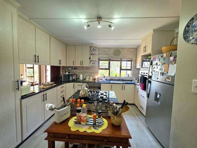 A functional kitchen featuring light-toned cabinetry, granite countertops, a central gas hob, and a tiled backsplash with ample natural light.