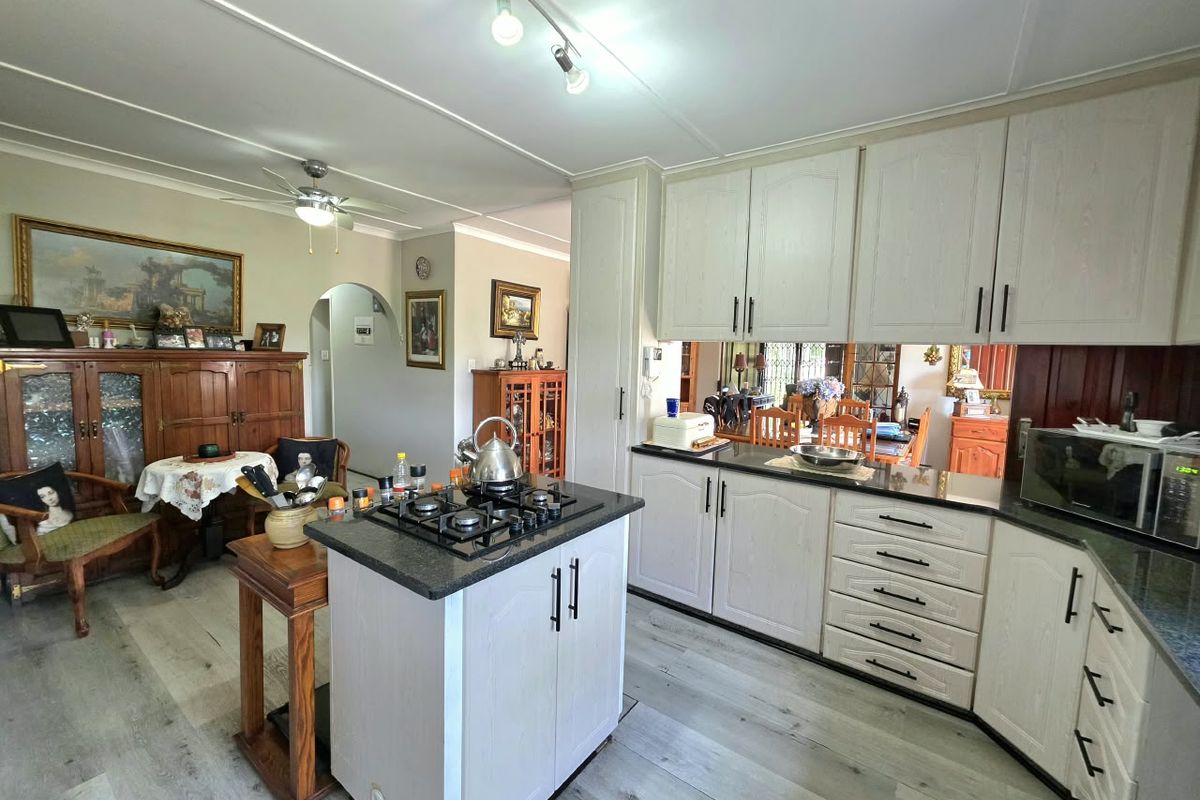 A functional kitchen featuring light-toned cabinetry, granite countertops, a central island with a gas hob, and modern laminate flooring.