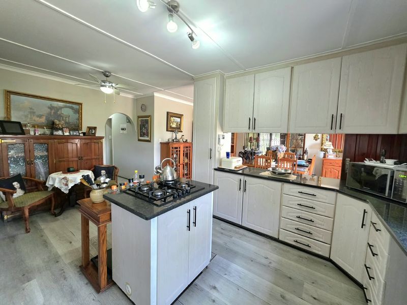 A functional kitchen featuring light-toned cabinetry, granite countertops, a central island with a gas hob, and modern laminate flooring.