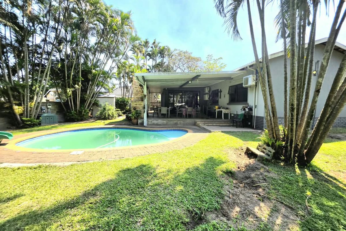 Rear garden view featuring a swimming pool, paved surround, and a covered patio area attached to the main house structure.
