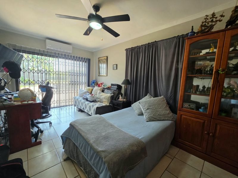 A functional bedroom featuring tiled flooring, a ceiling fan, and a wall-mounted split-system air conditioner, with direct access to an outdoor area via security gates.