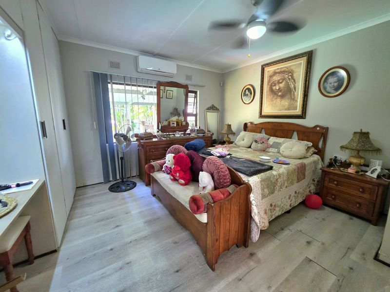 A spacious bedroom featuring laminate flooring, built-in cupboards, an air conditioning unit, and a ceiling fan, offering a comfortable and functional living space.
