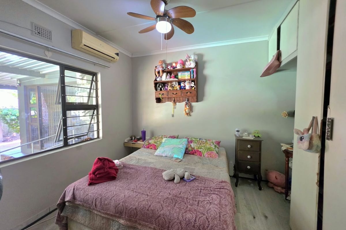 A functional bedroom featuring laminate flooring, a ceiling fan, split-system air conditioning, and built-in storage cupboards.