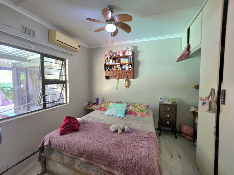 A functional bedroom featuring laminate flooring, a ceiling fan, split-system air conditioning, and built-in storage cupboards.