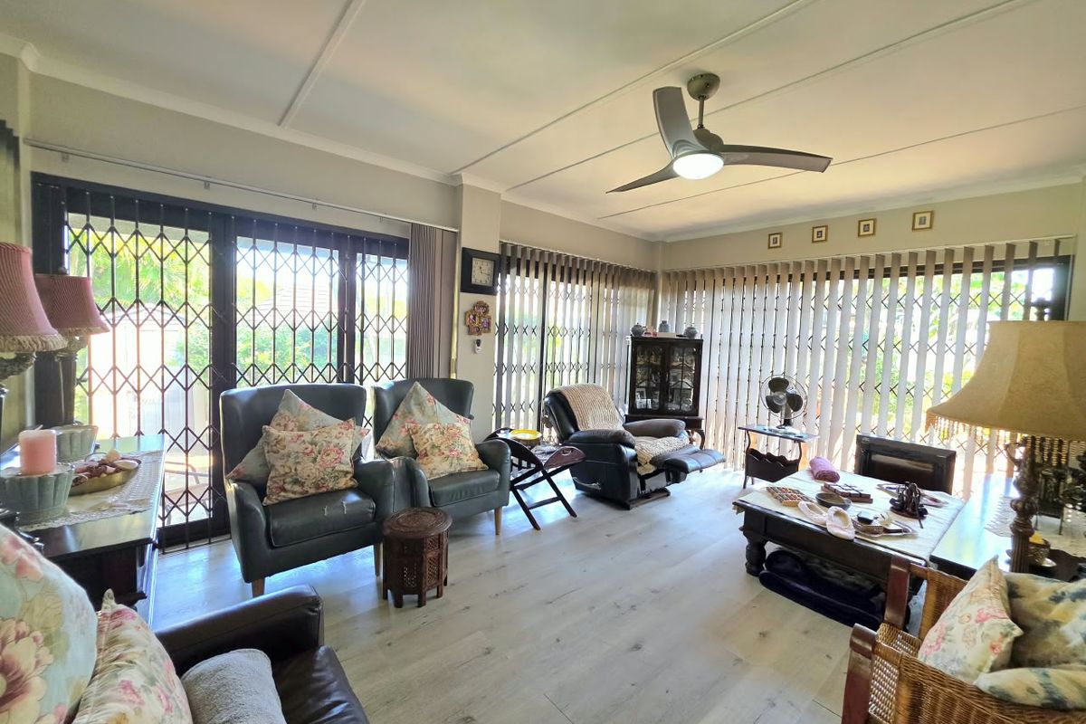 Spacious living room featuring light-toned laminate flooring, a modern ceiling fan, and large sliding doors secured with metal security gates and vertical blinds.