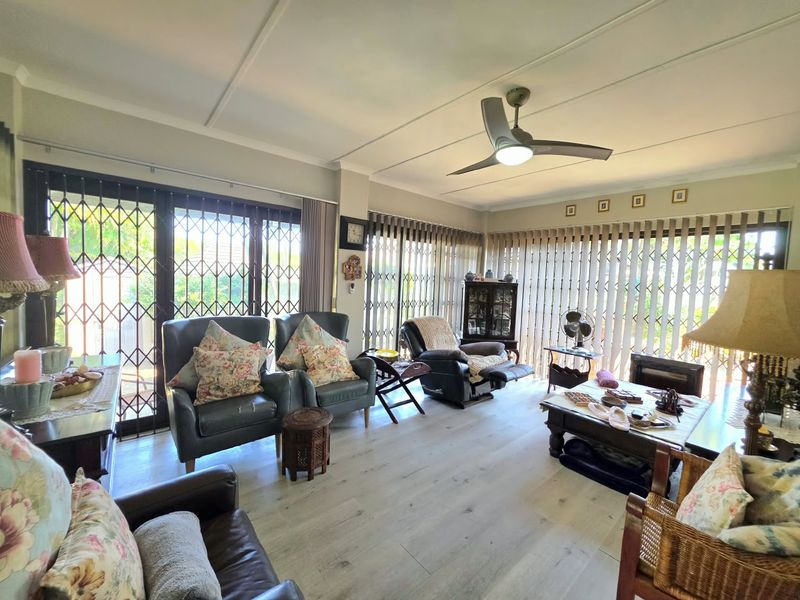 Spacious living room featuring light-toned laminate flooring, a modern ceiling fan, and large sliding doors secured with metal security gates and vertical blinds.
