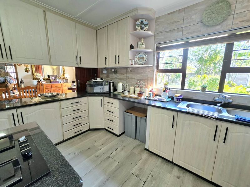 A functional kitchen featuring light-toned built-in cabinetry, dark granite countertops, a stainless steel sink, and durable laminate flooring with ample natural light.