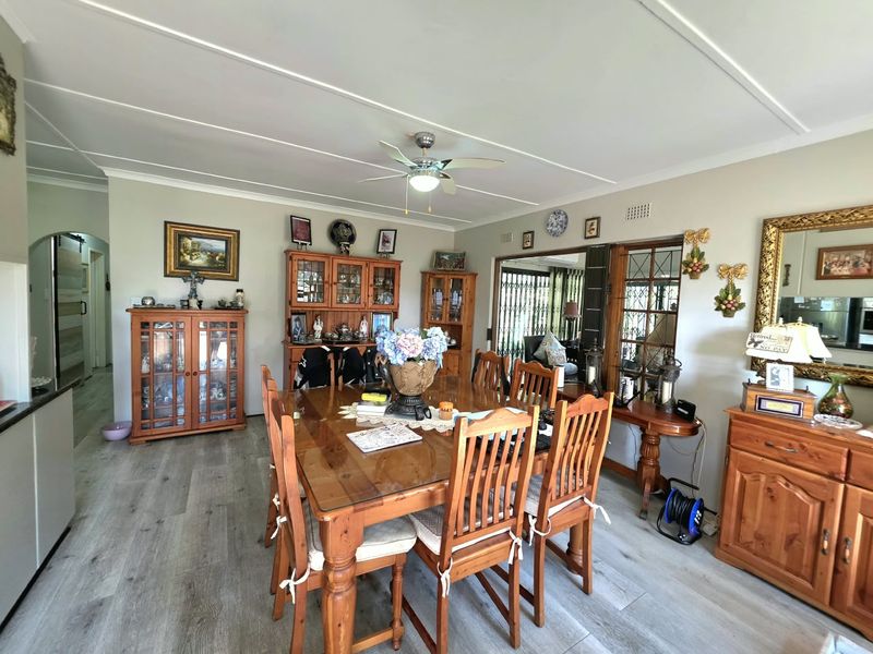 A spacious dining room featuring modern laminate flooring, a ceiling fan, and access to an adjacent room through a sliding door.