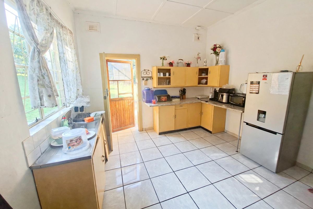 A functional kitchen featuring laminate cabinetry, tiled flooring, and direct access to the exterior through a timber door.