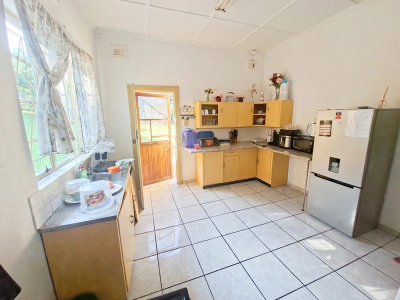 A functional kitchen featuring laminate cabinetry, tiled flooring, and direct access to the exterior through a timber door.