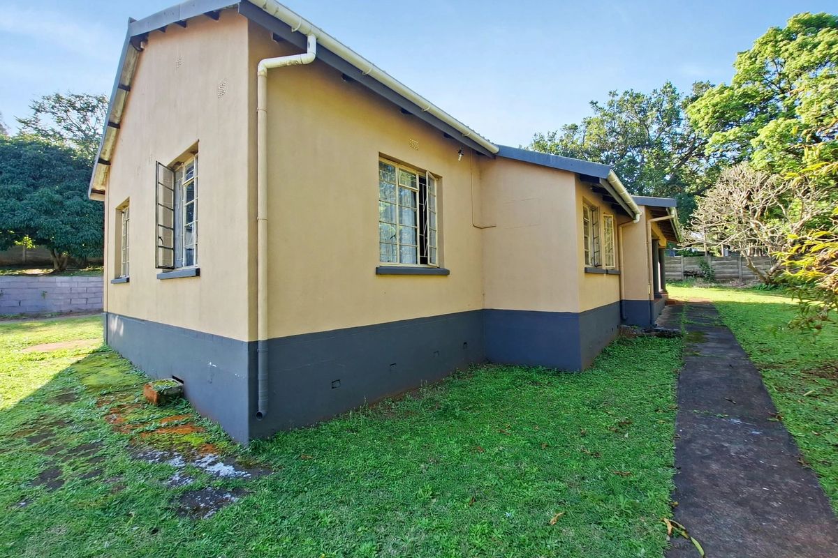 Rear exterior view of the house featuring plastered walls, steel-framed windows, and a surrounding garden with a concrete pathway.