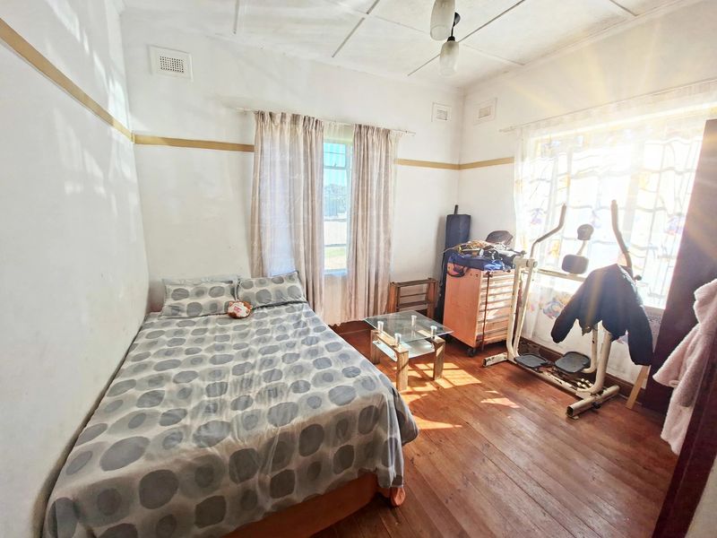 A bedroom featuring original hardwood flooring and high ceilings with visible wear, offering potential for renovation and modernization.