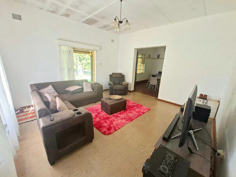 Spacious living room featuring tiled flooring and direct access to the garden through a sliding glass door, with an adjacent dining area visible.