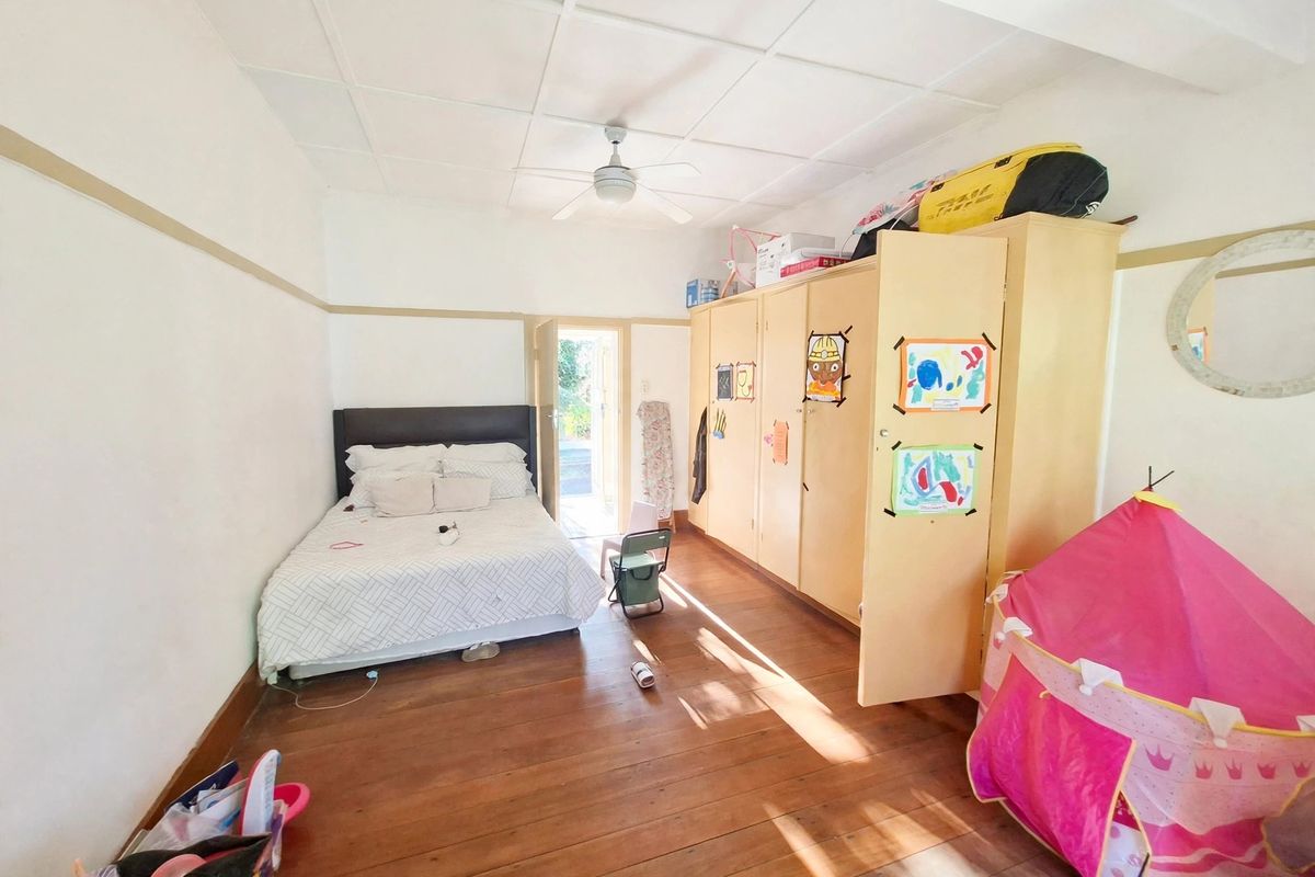 A bedroom featuring timber flooring, a ceiling fan, and extensive built-in cupboard storage with direct access to an outdoor area.