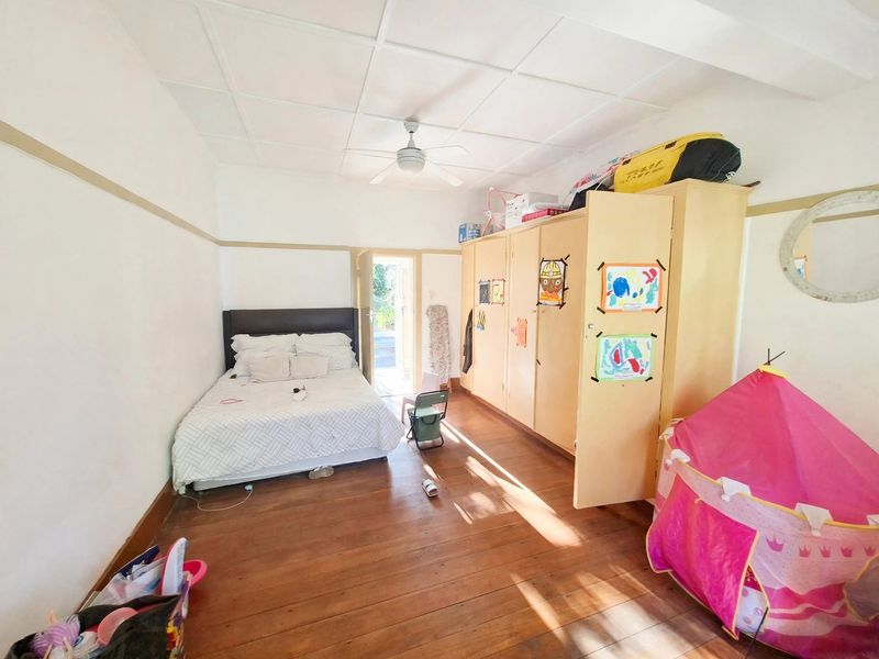 A bedroom featuring timber flooring, a ceiling fan, and extensive built-in cupboard storage with direct access to an outdoor area.