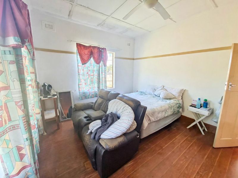 A bedroom featuring timber flooring, a ceiling fan, and a picture rail, requiring cosmetic updates to the ceiling and general finishes.