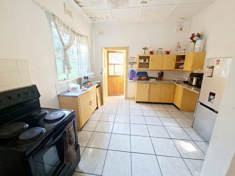 A dated kitchen featuring original cabinetry, tiled flooring, and a freestanding electric stove, with visible ceiling water damage requiring attention.