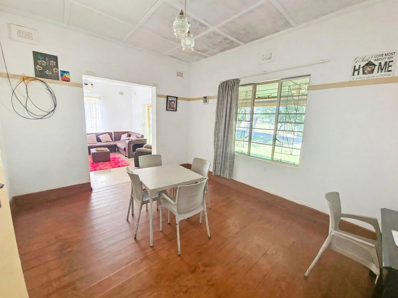 Dining room featuring timber flooring, steel-framed windows, and a ceiling with decorative tiles, leading into an adjacent living area.