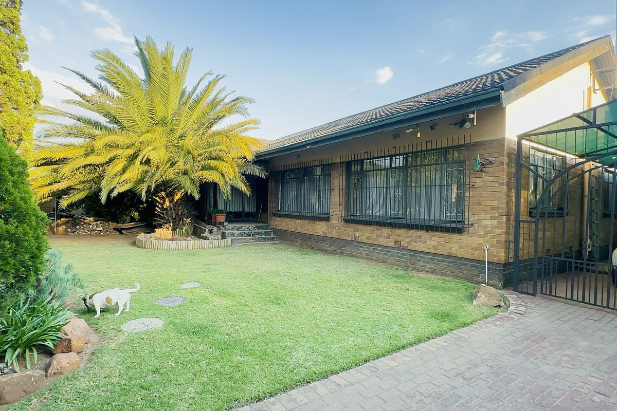 A well-maintained face brick home featuring a landscaped garden, mature palm tree, and a paved driveway with a covered carport.