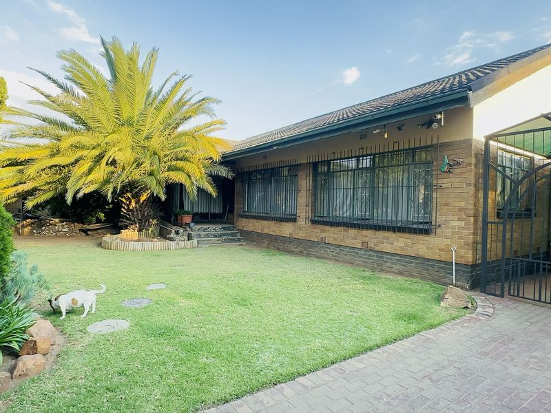 A well-maintained face brick home featuring a landscaped garden, mature palm tree, and a paved driveway with a covered carport.
