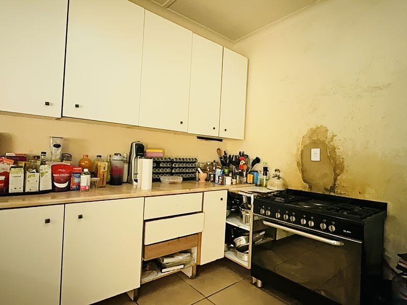 A dated kitchen featuring white cabinetry and a freestanding oven, currently showing significant wall surface damage and requiring cosmetic renovation.