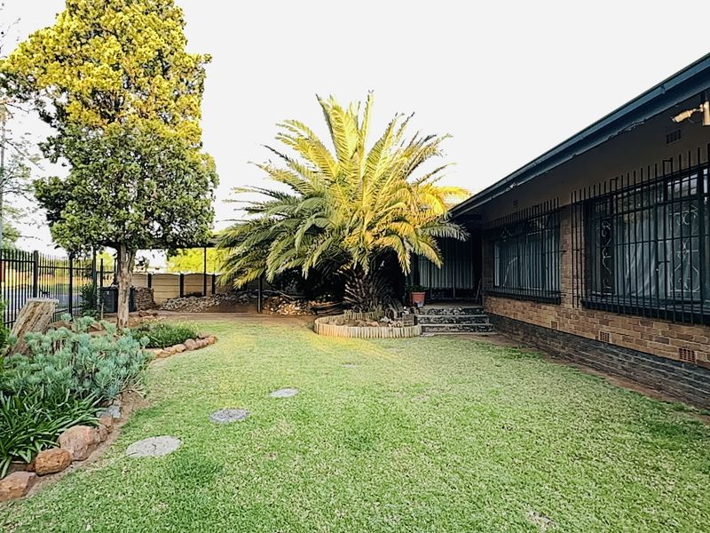 A well-maintained rear garden featuring a brick facade, established palm tree, and secure window bars, providing a private outdoor space.