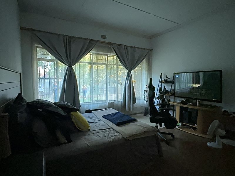 A bedroom featuring large windows with security bars and curtain fixtures, offering natural light and a view of the exterior.