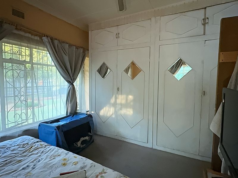 A bedroom featuring built-in cupboards with decorative mirror inserts and security bars on the windows.