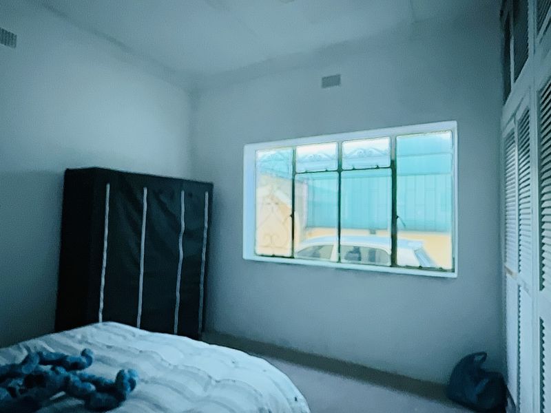 A bedroom featuring built-in cupboards with louvered doors and a large window providing natural light.