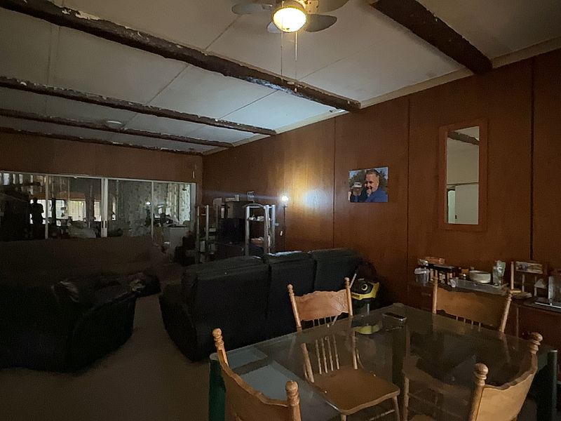 Open plan living and dining area featuring exposed timber ceiling beams, wood paneling, and sliding glass doors leading to an outdoor space.