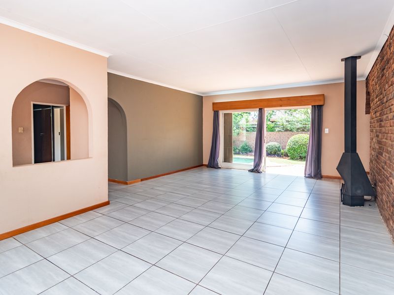 Spacious living area featuring tiled floors, an exposed brick feature wall, a freestanding fireplace, and sliding doors leading to the garden.