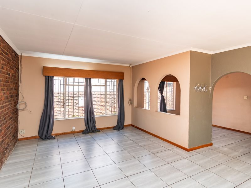 Spacious living area featuring tiled flooring, an exposed brick feature wall, and distinctive arched architectural details connecting to adjacent spaces.