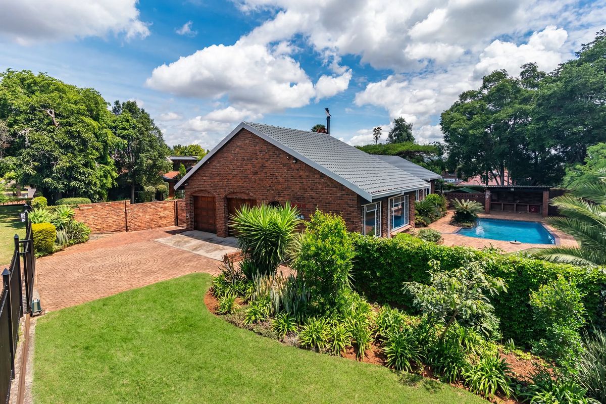 A well-maintained brick residence featuring a double garage, paved driveway, landscaped garden, and a private swimming pool in the rear yard.