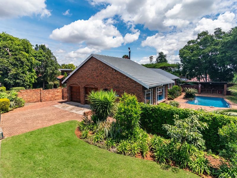A well-maintained brick residence featuring a double garage, paved driveway, landscaped garden, and a private swimming pool in the rear yard.