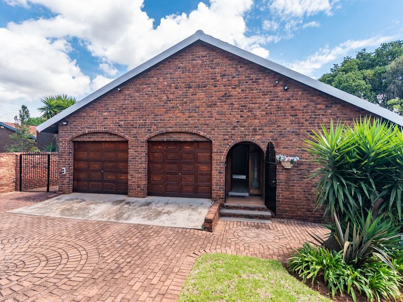Front view of a brick house featuring a double garage, arched entrance, and a paved driveway.